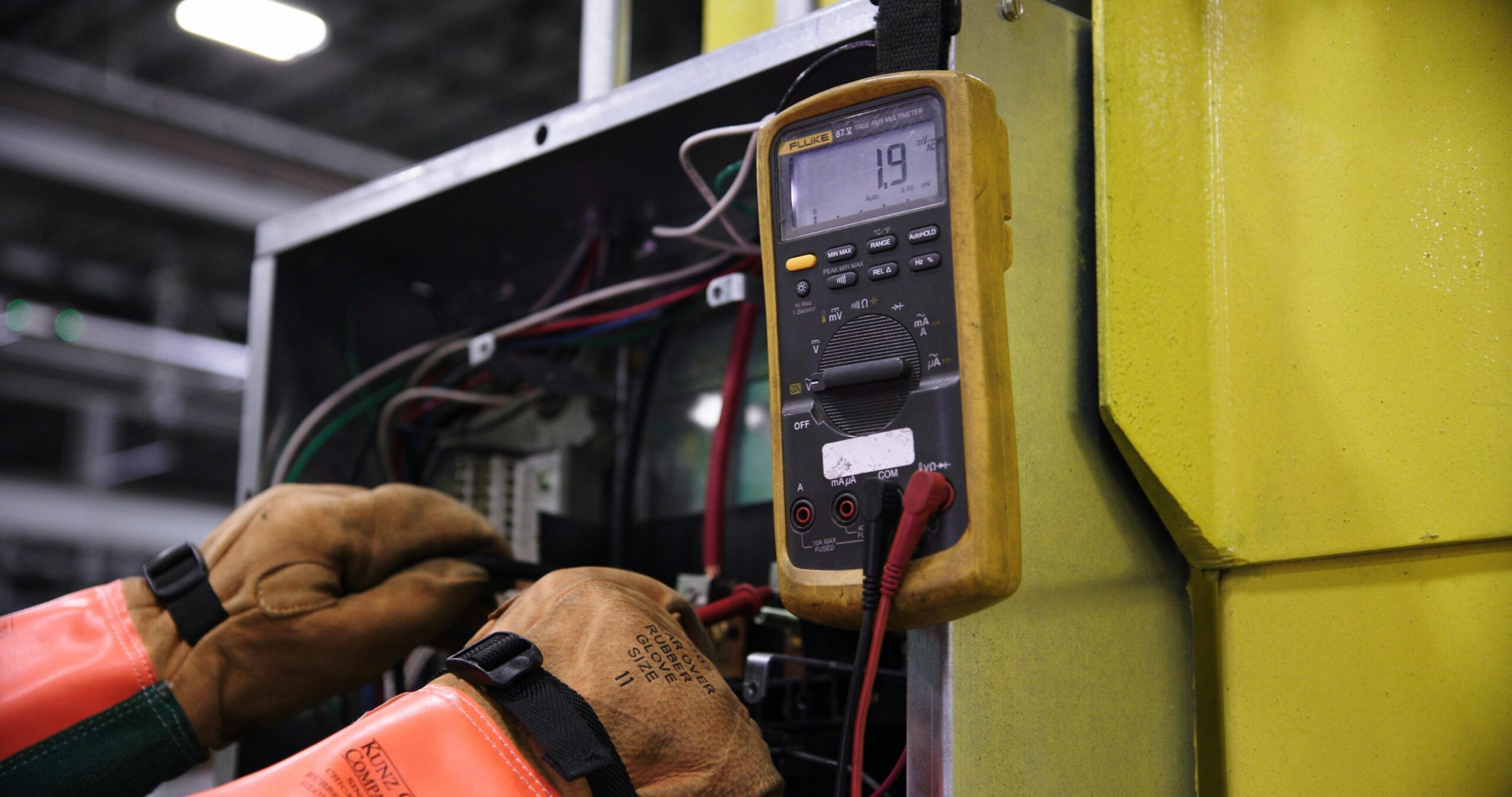 A technician in gloves and an orange vest checks electrical readings with a multimeter, focusing on Sydney home maintenance.
