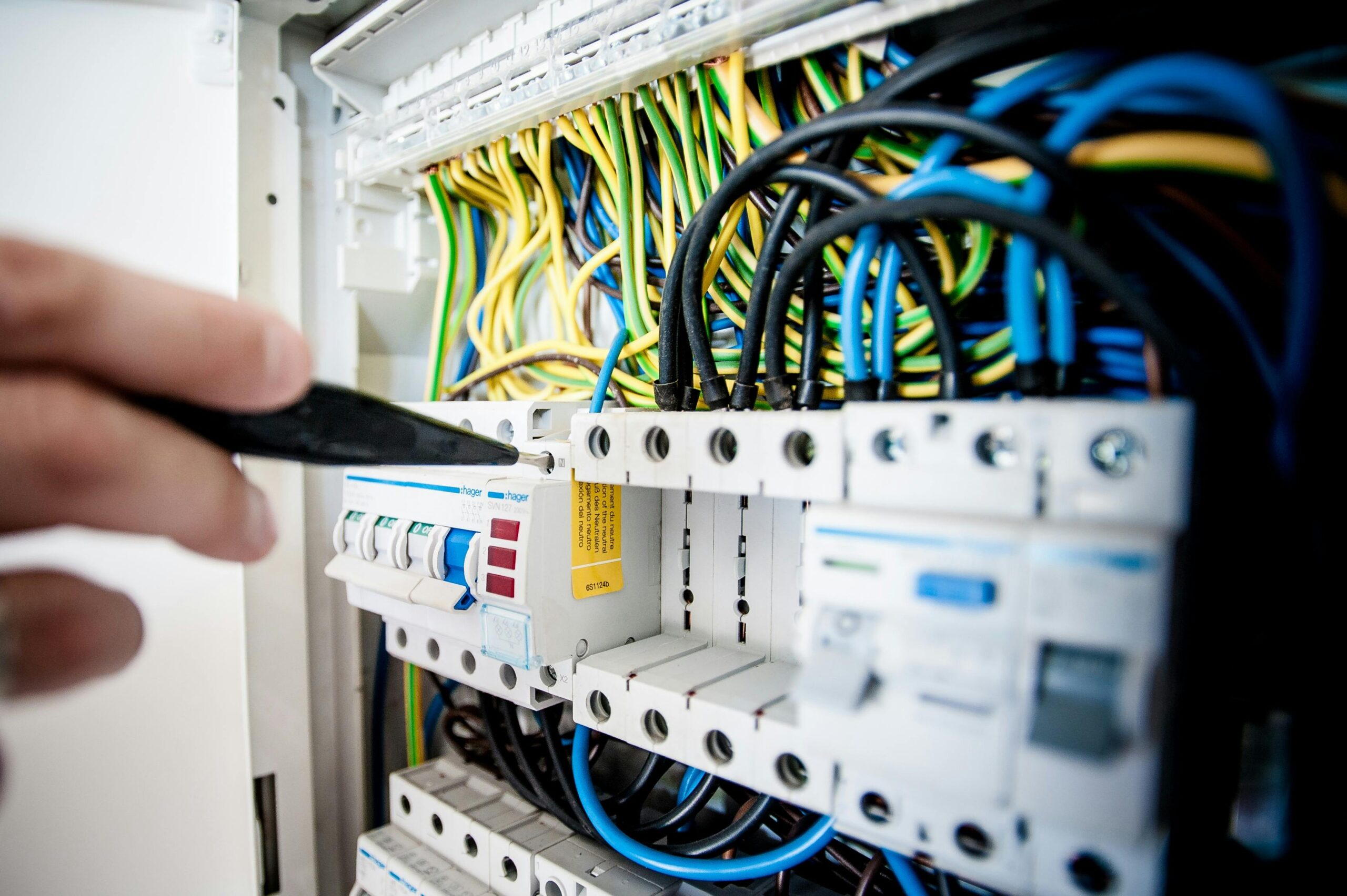 A technician examines an electrical panel with a screwdriver, showcasing maintenance practices for Sydney's electrical systems.